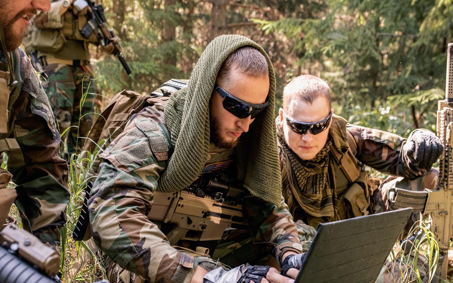 Men in camouflage gear working on a laptop in the field