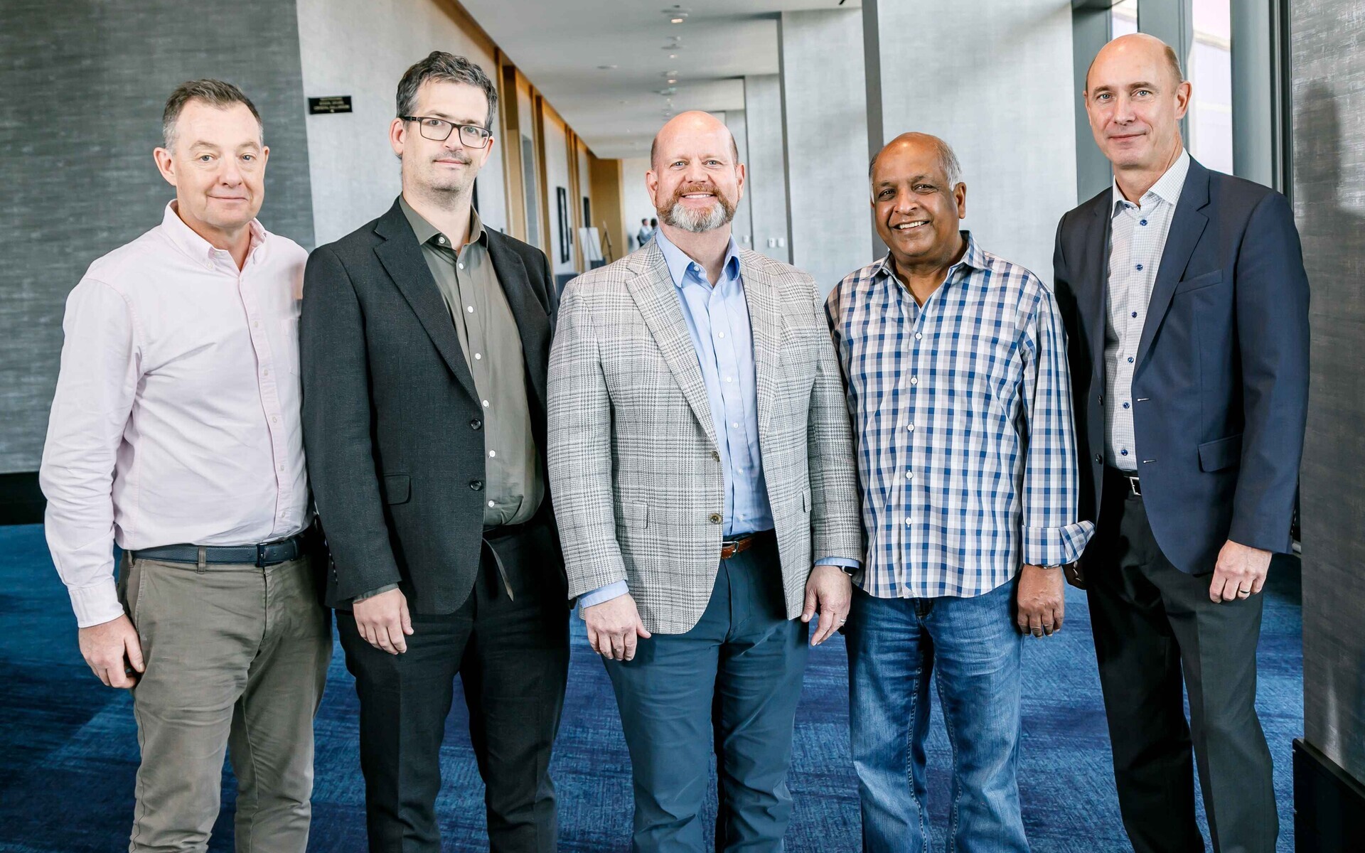 Five men in business attire stand and smile at the camera
