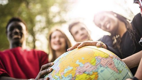 Multiple people with their hands on a globe
